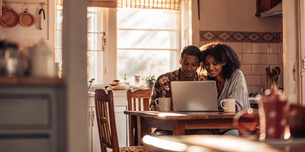 Young couple reviewing real estate listings on a laptop at their kitchen table