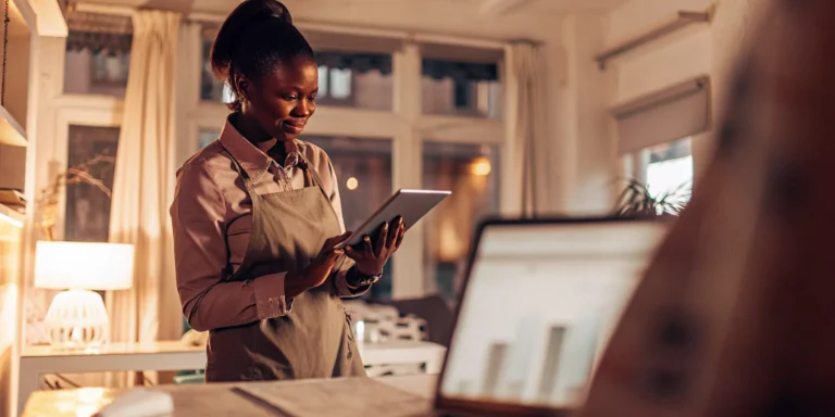 Self-employed business owner reviewing monthly financial statements in a bright modern home office with a mortgage comparison open on a laptop, in Visbl's clean blue and purple fintech style